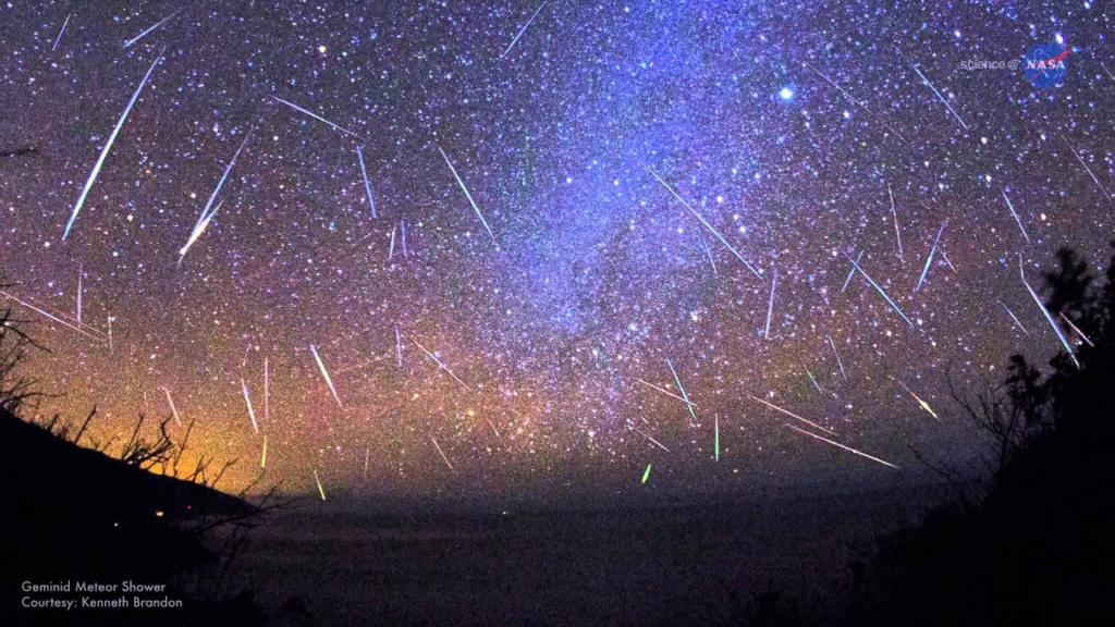 A vivid night sky filled with numerous meteors streaking across a backdrop of stars, with an illuminated horizon and hints of color in the atmosphere.