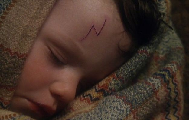 A sleeping child wrapped in a colorful blanket, with a distinctive lightning bolt-shaped mark on their forehead.