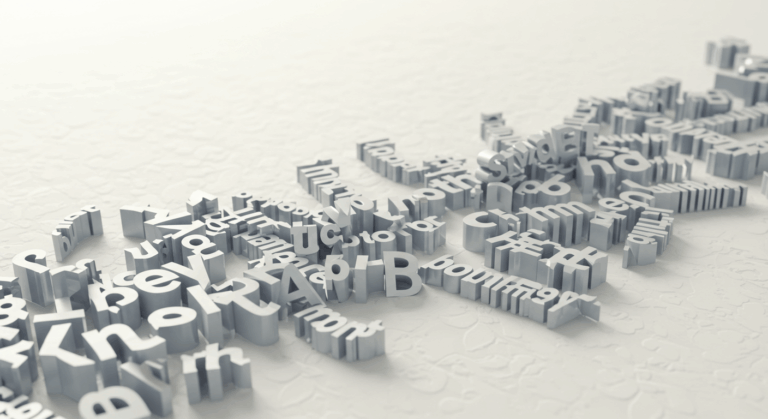 A scattered arrangement of three-dimensional gray letters positioned on a white textured surface, some letters standing upright while others lie flat, creating an abstract composition.